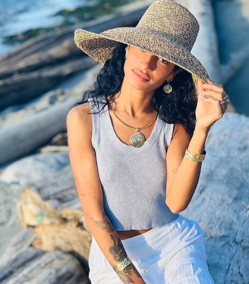 Woman wearing a wide-brimmed hat and sleeveless top on a beach.