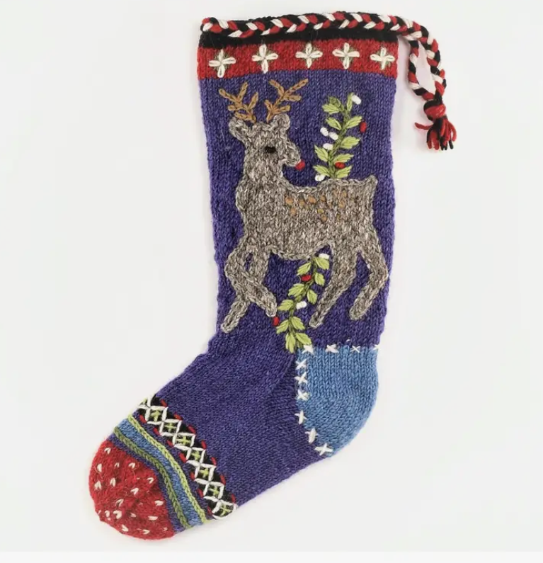 Hand-knitted Christmas stocking with embroidered reindeer and holly design, primarily in blue, red, and green colors, with a red cuff at the bottom.