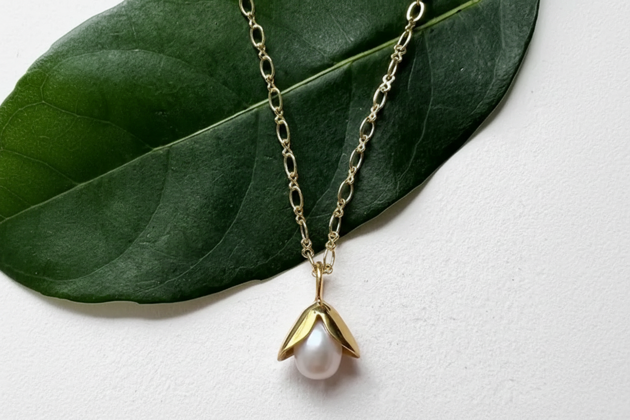 A freshwater pearl necklace with a brass setting in the shape of an acorn, displayed on a green leaf.