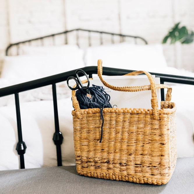 Woven basket with a black handle on a bed with a white background
