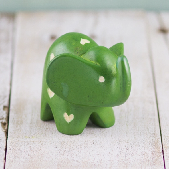 A hand-carved green Kisii stone elephant with white spots and hearts on a wooden surface.