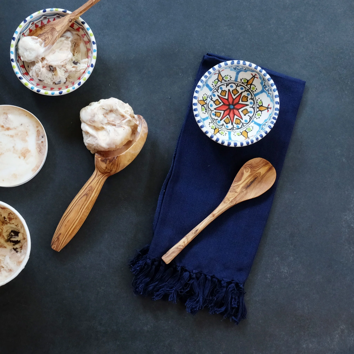 Wooden spoons with ice cream next to a colorful ceramic plate on a dark surface