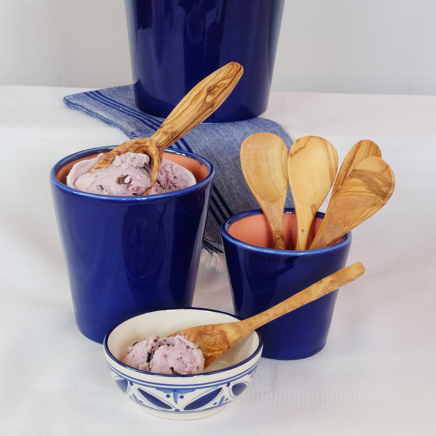 Blue ceramic cups with pink ice cream and wooden spoons on a white surface.