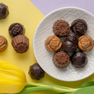 Switch Assorted chocolates on a white plate with a yellow tulip on a yellow and purple background 2 image