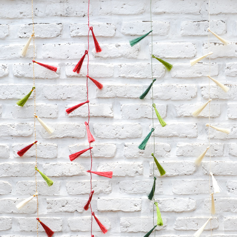 Colorful tassel garland hanging against a white brick wall.