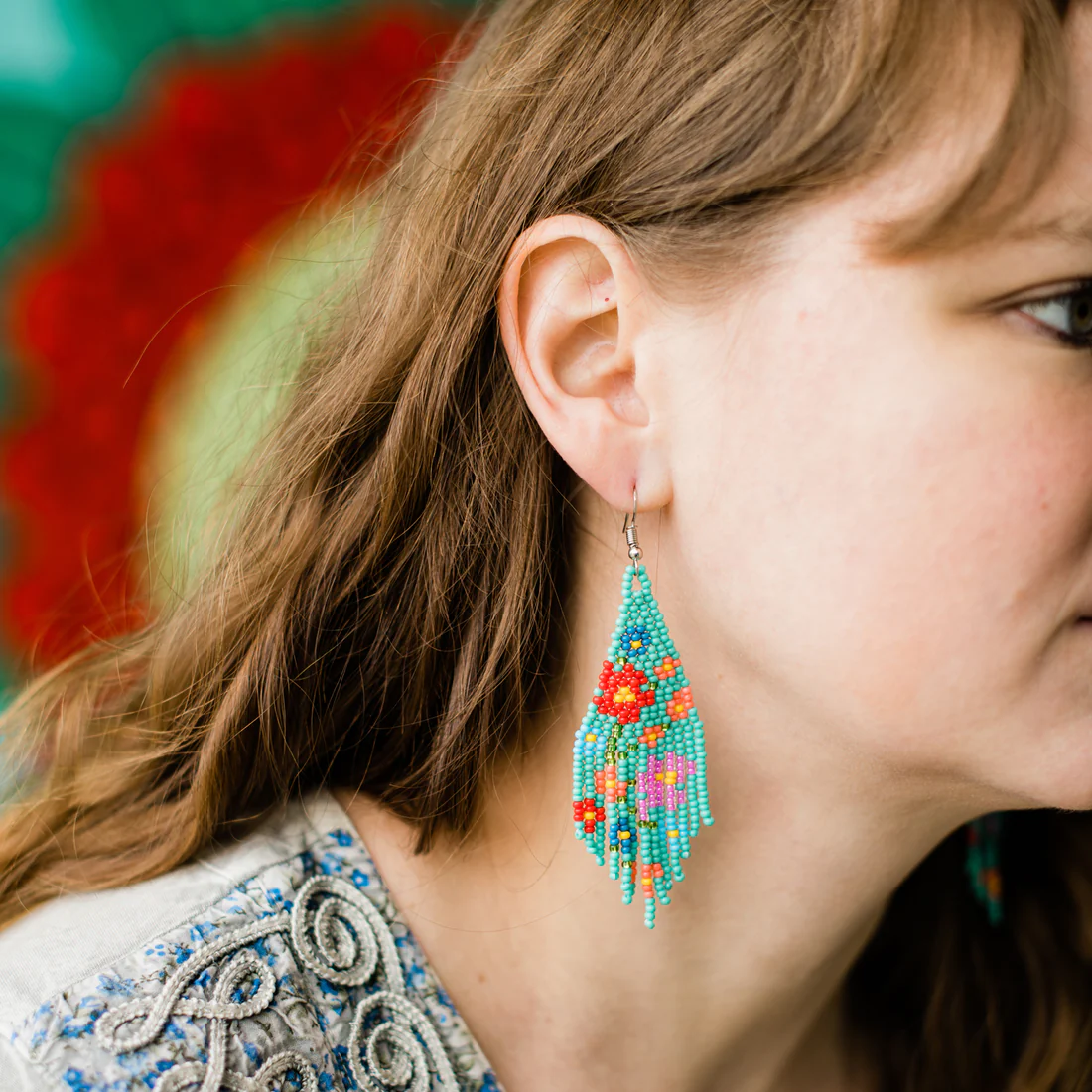 Close-up of a woman wearing colorful beaded earrings with a blurred floral background.