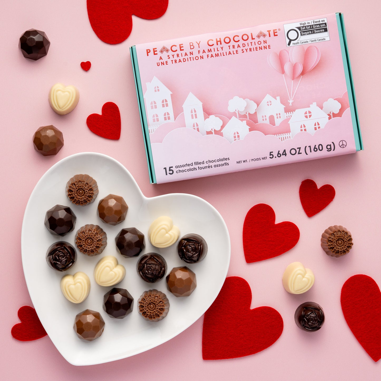 Assorted chocolates on a heart-shaped plate with a 'Peace by Chocolate' box on a pink background with red hearts.