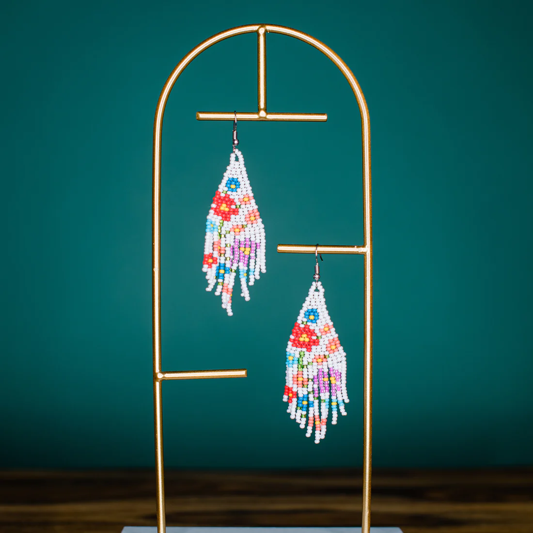 Colorful beaded earrings on a gold stand against a teal background