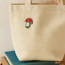 Switch Beige tote bag with a decorative mushroom pin charm on top of books 2 image