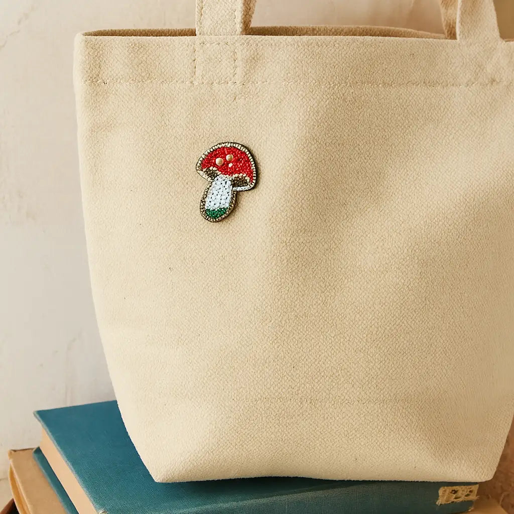 Beige tote bag with a decorative mushroom pin charm on top of books