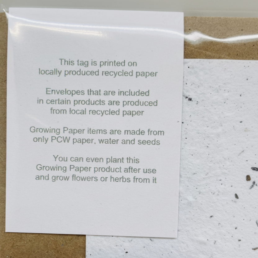 White tag on a textured paper background with text about locally produced recycled paper and plantable products.