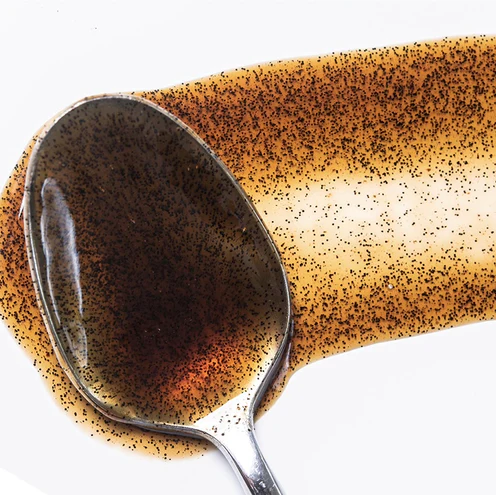 Metallic spoon spreading vaniila bean paste on a white background